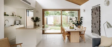 Open-plan kitchen and dining space with a raked timber-lined ceiling and polished concrete floor, opening to the garden.