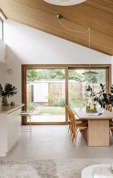 Open-plan kitchen and dining space with a raked timber-lined ceiling and polished concrete floor, opening to the garden.