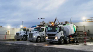 Holcim concrete mixer trucks at the mobile batch plant on Melbourne Airport's Taxiway Zulu 2.0 project, with an aircraft taking off in the background.