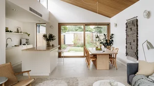 Open-plan kitchen and dining space with a raked timber-lined ceiling and polished concrete floor, opening to the garden.
