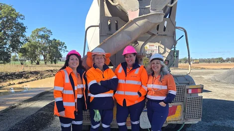 Four women in hi-vis workwear and hard hats stand together in front of a concrete agitator truck on a construction site in Central West NSW.