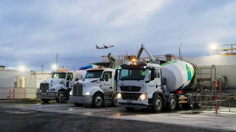 Holcim concrete mixer trucks at the mobile batch plant on Melbourne Airport's Taxiway Zulu 2.0 project, with an aircraft taking off in the background.