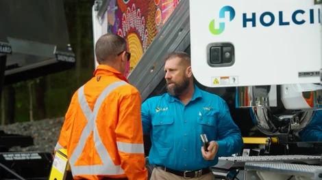 Nathan Turner from True Blue Transport speaking with a worker in high-visibility clothing beside a Holcim-branded truck.