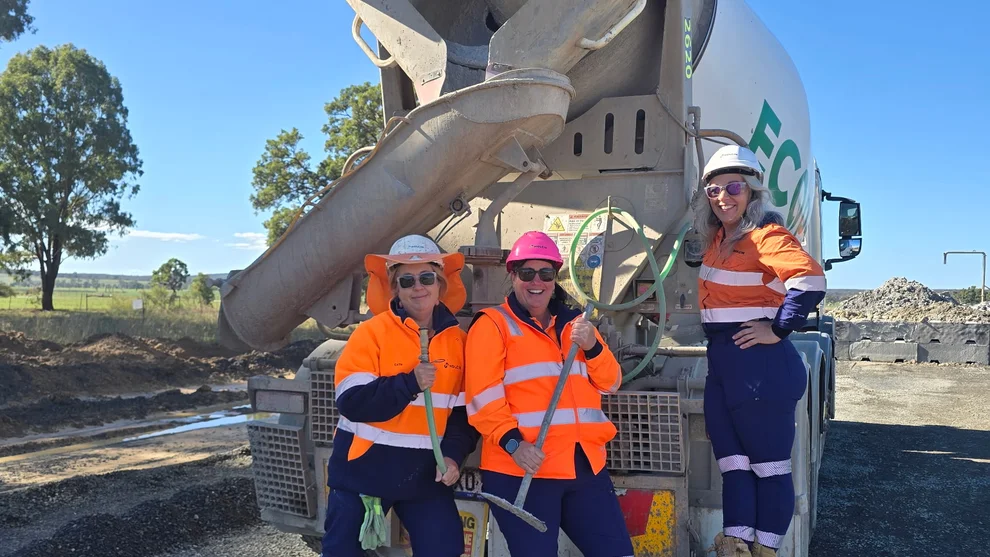 Three Women on Wheels participants in hi-vis workwear and hard hats pose with slump rods in front of a concrete agitator truck at the Central-West Orana Renewable Energy Zone site, Central West NSW.