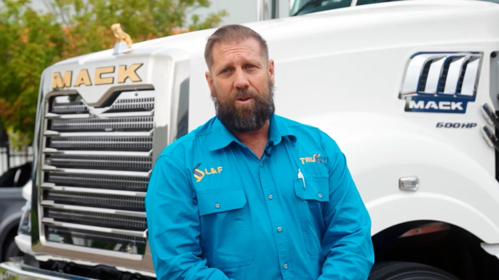 Nathan Turner from True Blue Transport Group speaking in front of a Mack truck, wearing a branded blue work shirt.