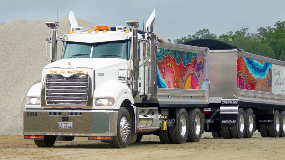 Holcim-branded Mack heavy haulage truck and trailer with Indigenous artwork design, parked on a gravel site in Queensland.