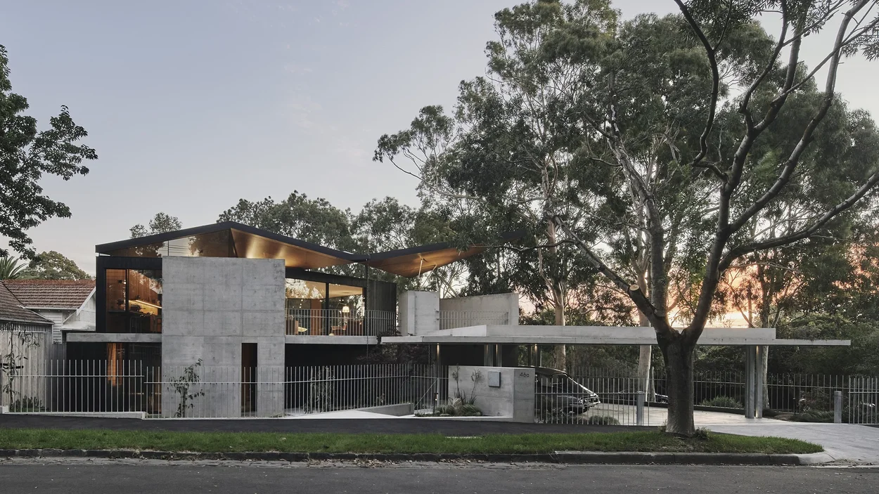 Two-storey Hawthorn home at dusk, with off-form Architectural Grey concrete walls and a cantilevered concrete slab set among established gum trees.